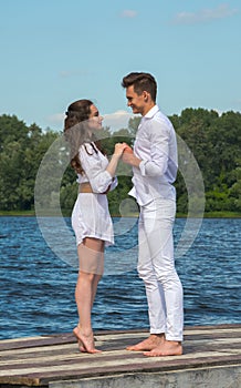 Man and woman holding hands on a wooden pier near the water.