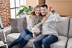 Man and woman holding key sitting on sofa with dog at new home