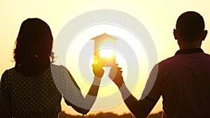 A man and a woman holding a paper house and watching the sunset. Silhouette of a happy family. Prenup, family