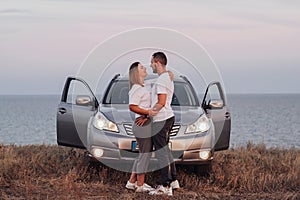 Man and Woman Hugging in Front of Their SUV Car, Young Couple Standing Together on the Background of Sea, Road Trip
