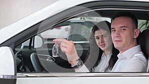 A man and a woman are inside a vehicle. The man holds the car key while sitting next to the automotive mirror.