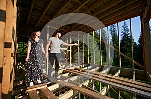 Man and woman inspecting their future wooden frame house nestled in the mountains near forest.