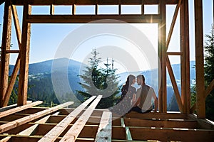 Man and woman inspecting their future wooden frame house nestled in the mountains near forest.
