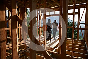 Man and woman inspecting their future wooden frame house nestled in the mountains near forest.