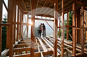 Man and woman inspecting their future wooden frame house nestled in the mountains near forest.