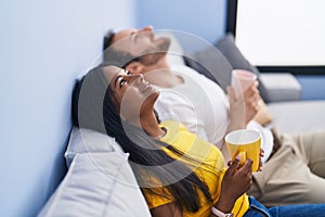 Man and woman interracial couple drinking coffee sitting on sofa at home