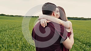 A man and a woman are joining hands, walking in a field, hugging and kissing. Slow mo, steadicam shot.