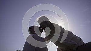 A man and a woman kiss against the background of the hard backdrop of the sun