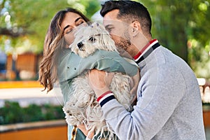 Man and woman kissing dog sitting together at park