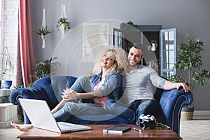 Man and woman with laptop sitting on a blue sofa at home. Young family planning