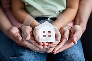 Man, woman and little child holding cutout paper house figure in hands