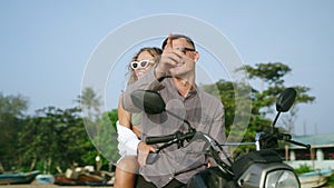 Man, woman in love sit on motorcycle by sea on beach, enjoy sunset. People enjoy view, pointing with hand sitting on