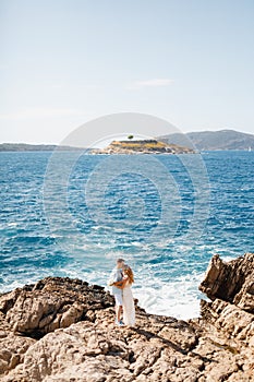 Man and woman in love stand embracing and holding hands on the rocky seashore, behind them is the Mamula island