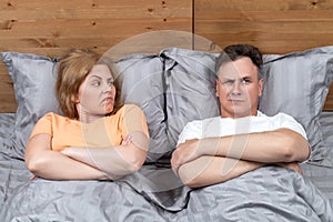 Man and a woman are lying in bed under a gray blanket, she looks at him with displeasure. Relationship concept