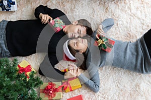 Man and woman lying on carpet on the floor in Christmas decorated room with Christmas tree and box