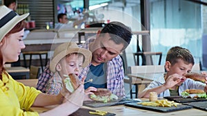 Man and woman with male children enjoy eating tasty juicy burgers with fries sitting at table in cafe