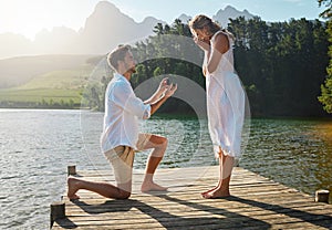 Man, woman and marriage proposal by lake on vacation with surprise, wow or happiness in sunshine. Couple, engagement and