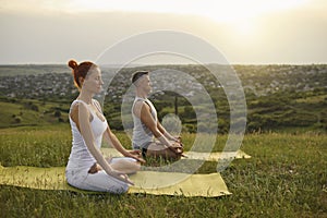 Man and woman meditating in countryside at sunset