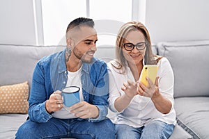 Man and woman mother and son using smartphone drinking coffee at home