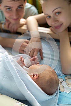 Man and a woman near their newborn. Parents look at the camera. Boy sleeping in his crib. Mom, dad and baby. Portrait of young