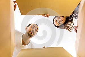 Man and woman opening a carton box and looking inside, surprised and curious.