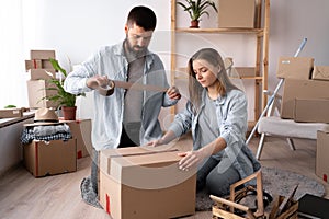 Man and woman packing on moving day. guy sealing a cardboard box with tape, moving and relocation concept