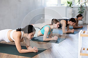 Man and woman performing Bhujangasana or Cobra pose during yoga class with group in fitness studio