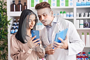 Man and woman pharmacist and client using smartphone and touchpad at pharmacy