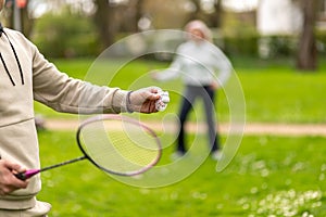 Man and woman playing badminton outdoors, focus on hand with shuttlecock