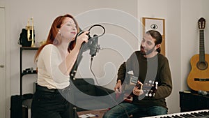 Man and woman playing guitar singing song at music studio