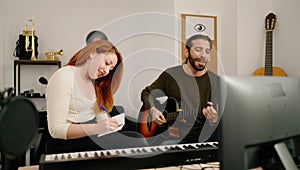 Man and woman playing guitar writing on notebook at music studio