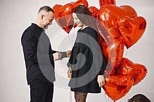 Man and woman posing in studio near bunch of heart-shaped red ballons
