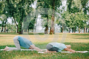 Man and woman practicing relaxation yoga poses on yoga mats on lawn