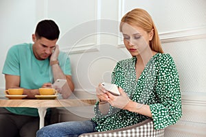 Man and woman preferring smartphones over speaking with each other during first date in cafe photo