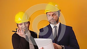 Man and woman professional architects with hard hats, tablet and walkie talkie isolated on orange background