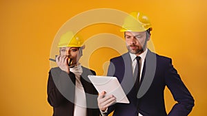 Man and woman professional architects with hard hats, tablet and walkie talkie isolated on orange background