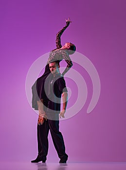 Man and woman, professional tango, ballroom dancers in stylish, beautiful stage posing over purple background on neon