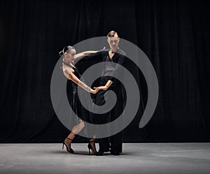 Man and woman, professional tango dancers performing in black stage costumes over black background. Choreography. Dance