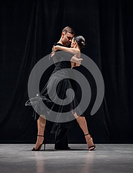 Man and woman, professional tango dancers performing in black stage costumes over black background. Couple dance