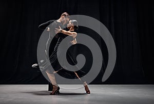 Man and woman, professional tango dancers performing in black stage costumes over black background. Expression of