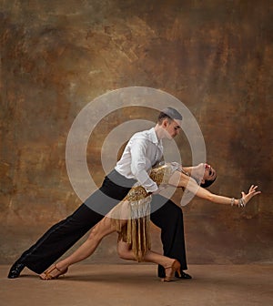Man and woman, professional tango dancers in stylish, beautiful stage costumes performing over dark vintage background