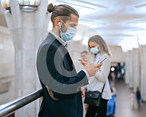 man and a woman in protective masks waiting for a train in the subway.