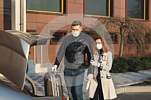 Man and woman in protective medical masks and gloves leave the house by car during the quarantine.
