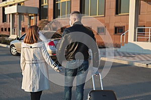 Man and woman in protective medical masks and gloves with a suitcase leave the house by car during the quarantine and