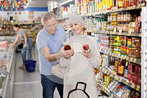 Man and woman purchasers choosing tomato juice in big supermarket