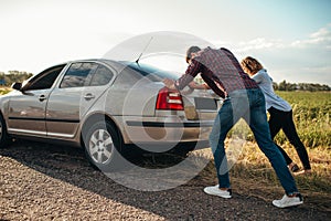 Man and woman pushing a broken car, back view