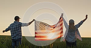 A man and a woman raise the US flag over a field of wheat as the sun sets. USA independence day concept
