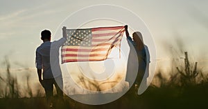 Man and woman raising the US flag over a field of wheat at sunset