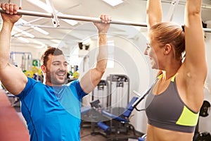 Man and woman reaching up to monkey bars at a gym