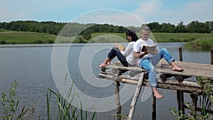 Man and woman reading books on the board table near lake